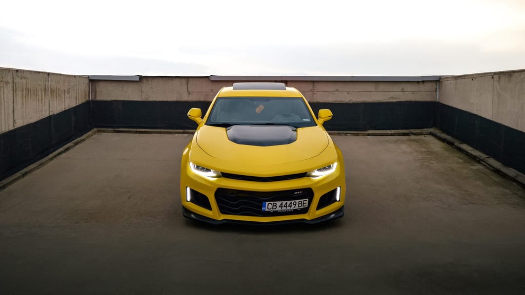 Жълт Chevrolet Camaro SS отпред, със светнали фарове, на бетонен покрив